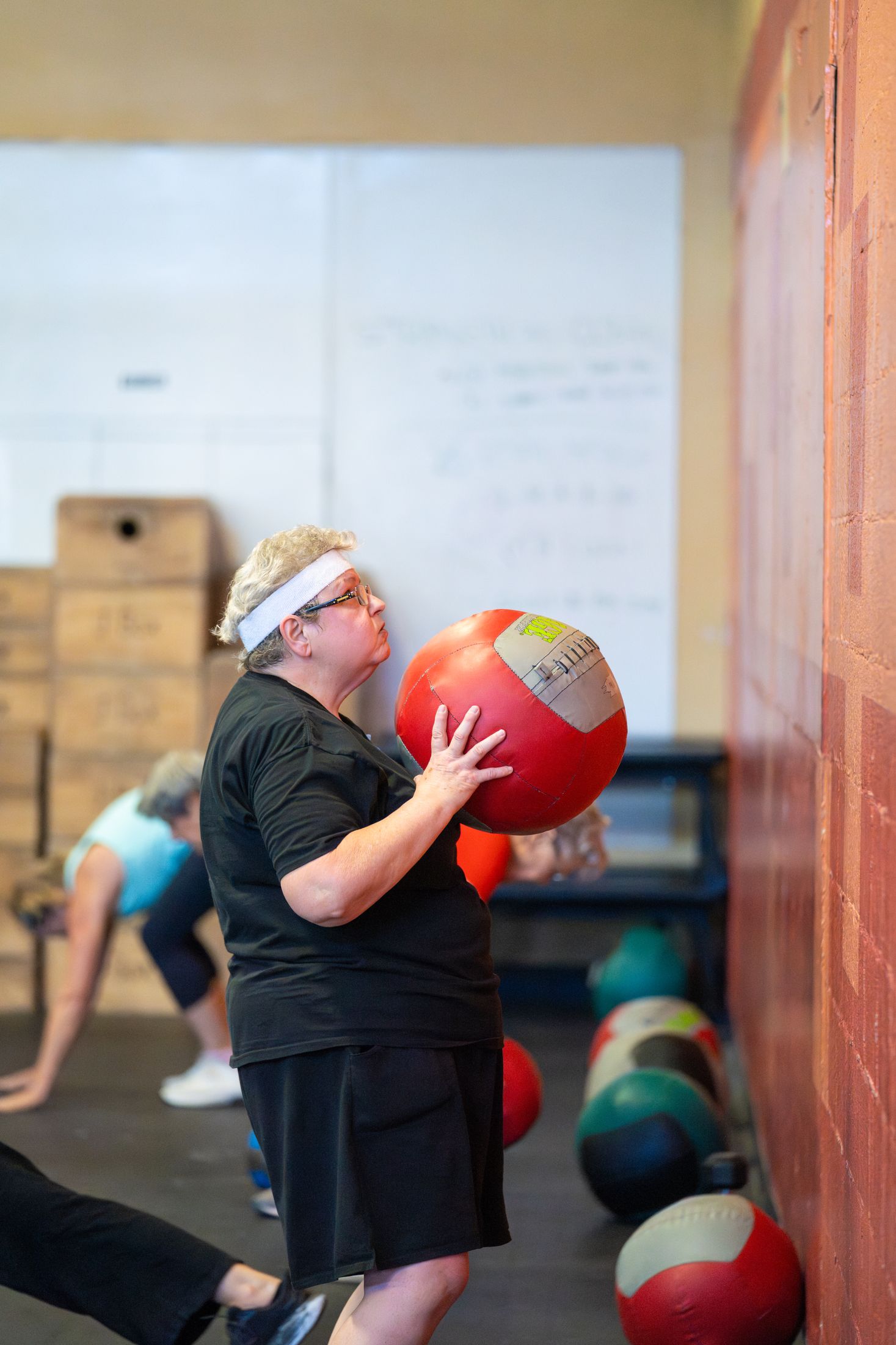 A participant hugs a red medicine ball in a squat